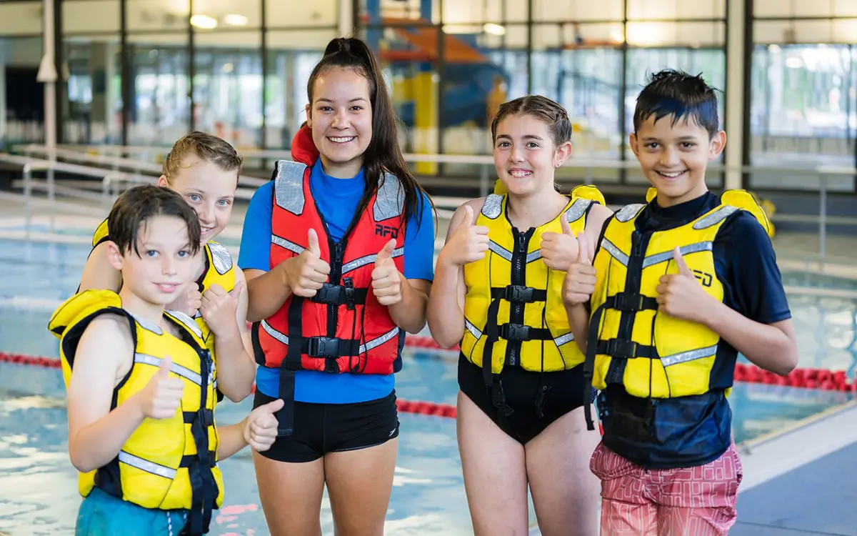 A group of children in yellow life jackets and an instructor giving thumbs up at Christchurch Recreation and Sport pool.