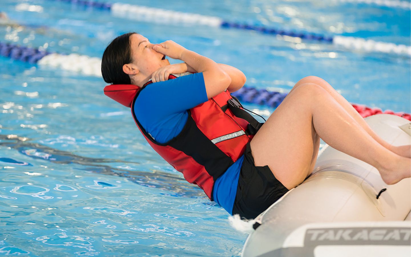 An instructor in a red lifejacket demonstrating falling out of a raft at Christchurch Recreation and Sport pool. 