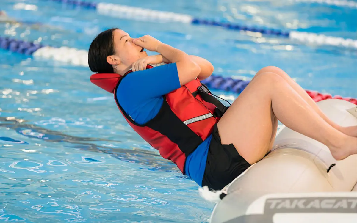 An instructor in a red lifejacket demonstrating falling out of a raft at Christchurch Recreation and Sport pool.