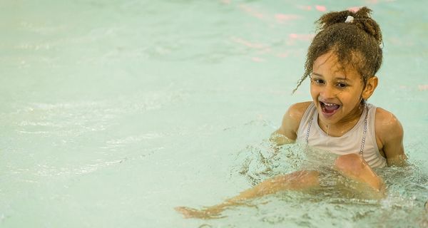 A smiling little girl sitting in the toddler's pool at Christchurch Recreation and Sport pool. 