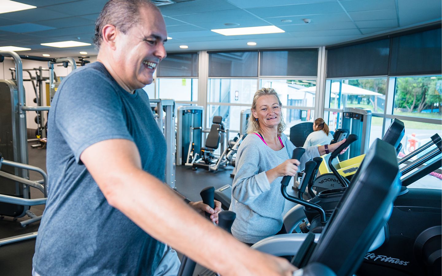 A smiling man and woman participating in an elliptical workout at Christchurch Recreation and Sport Centre. 