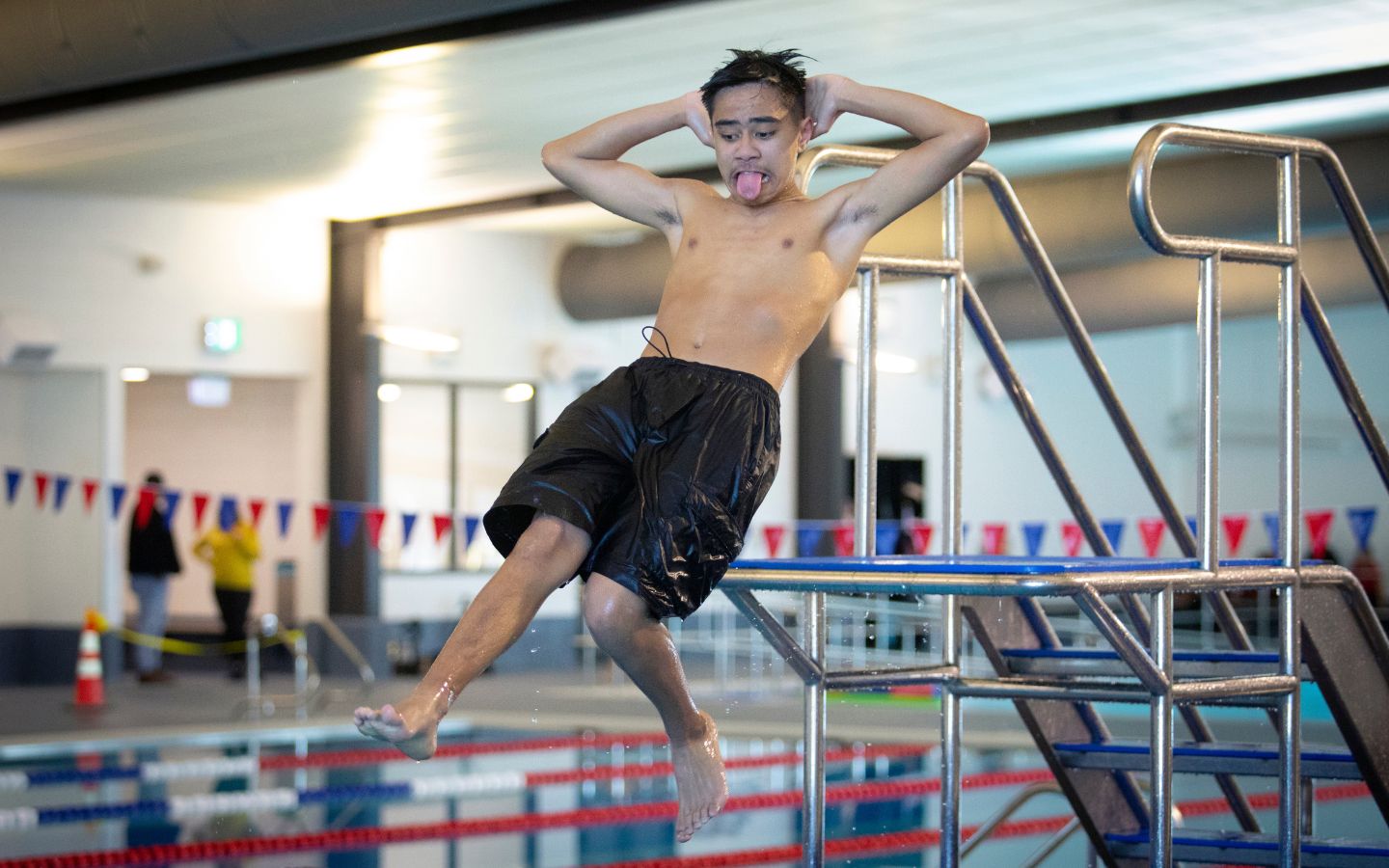 A teenage boy doing a manu off a diving board at Christchurch Recreation and Sport pool. 