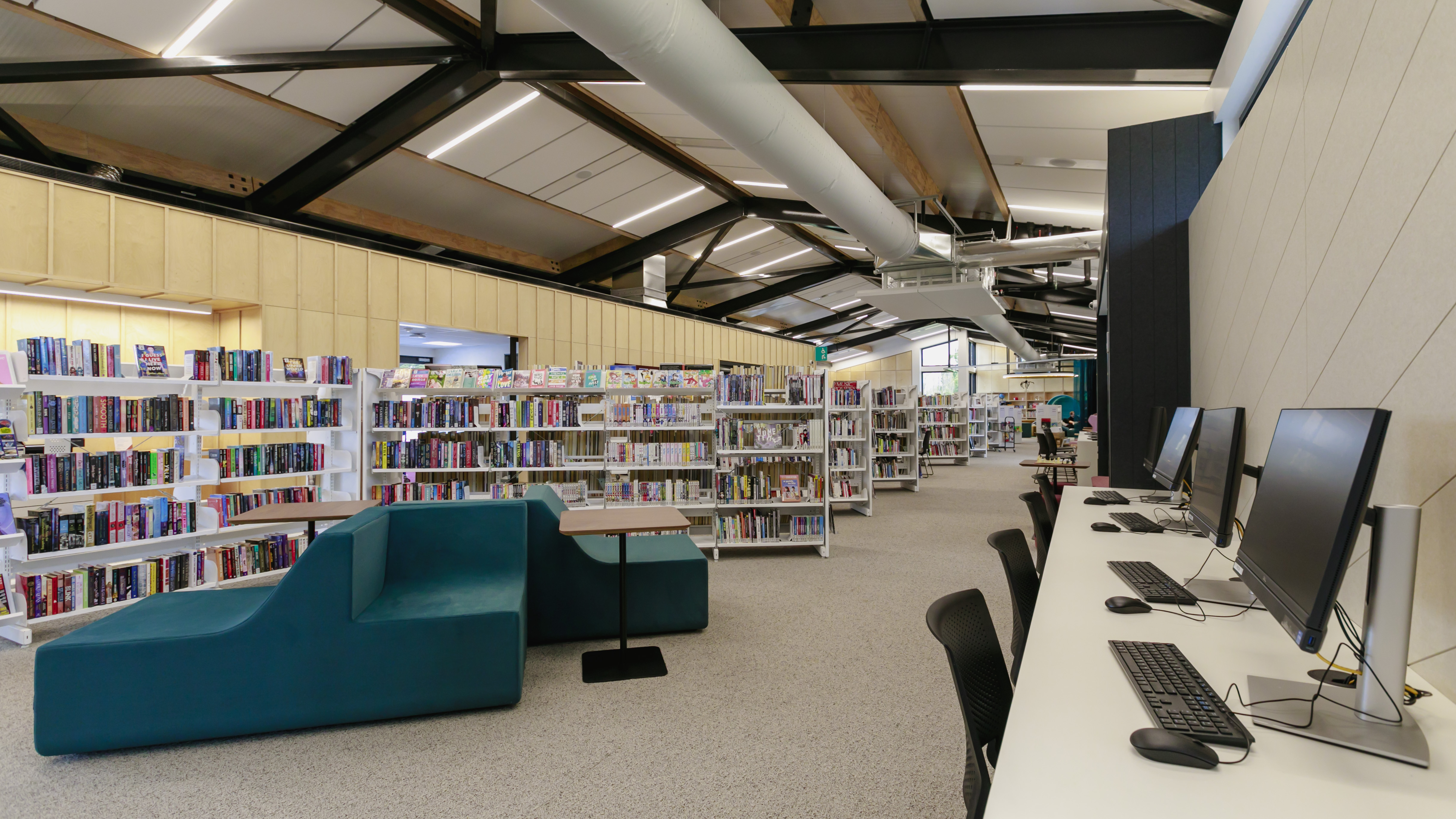 The Matatiki Hornby library reading and computer area equipped with white shelves of books, green couches and a wall of desktop computers along the parrel wall. 