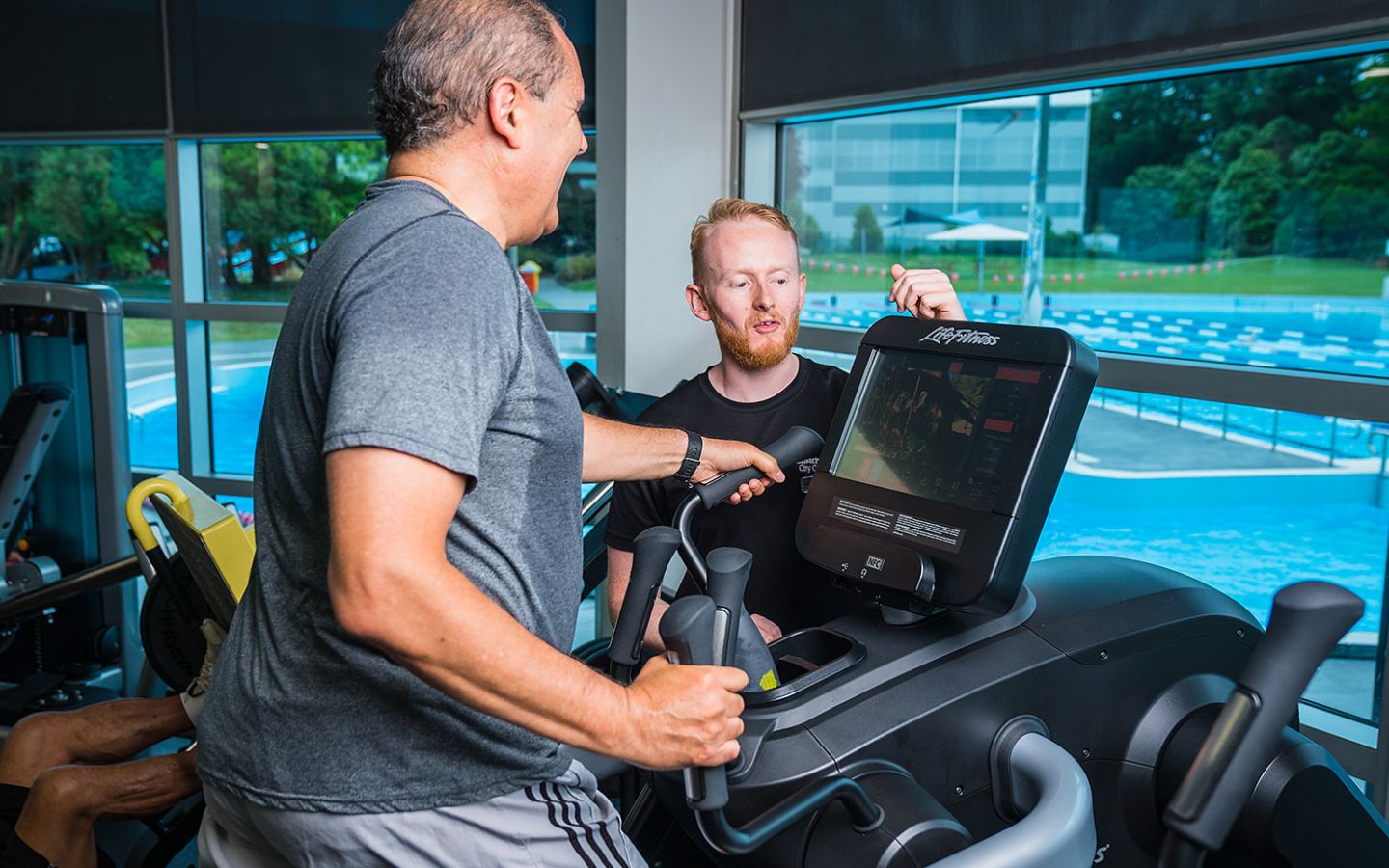 A male personal trainer assisting a man in blue with a treadmill workout at Christchurch Recreation and Sport Centre. 