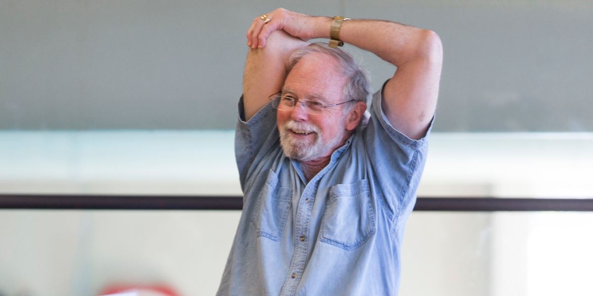 A smiling older man stretching during a seated gentle exercise class at Christchurch Recreation and Sport.