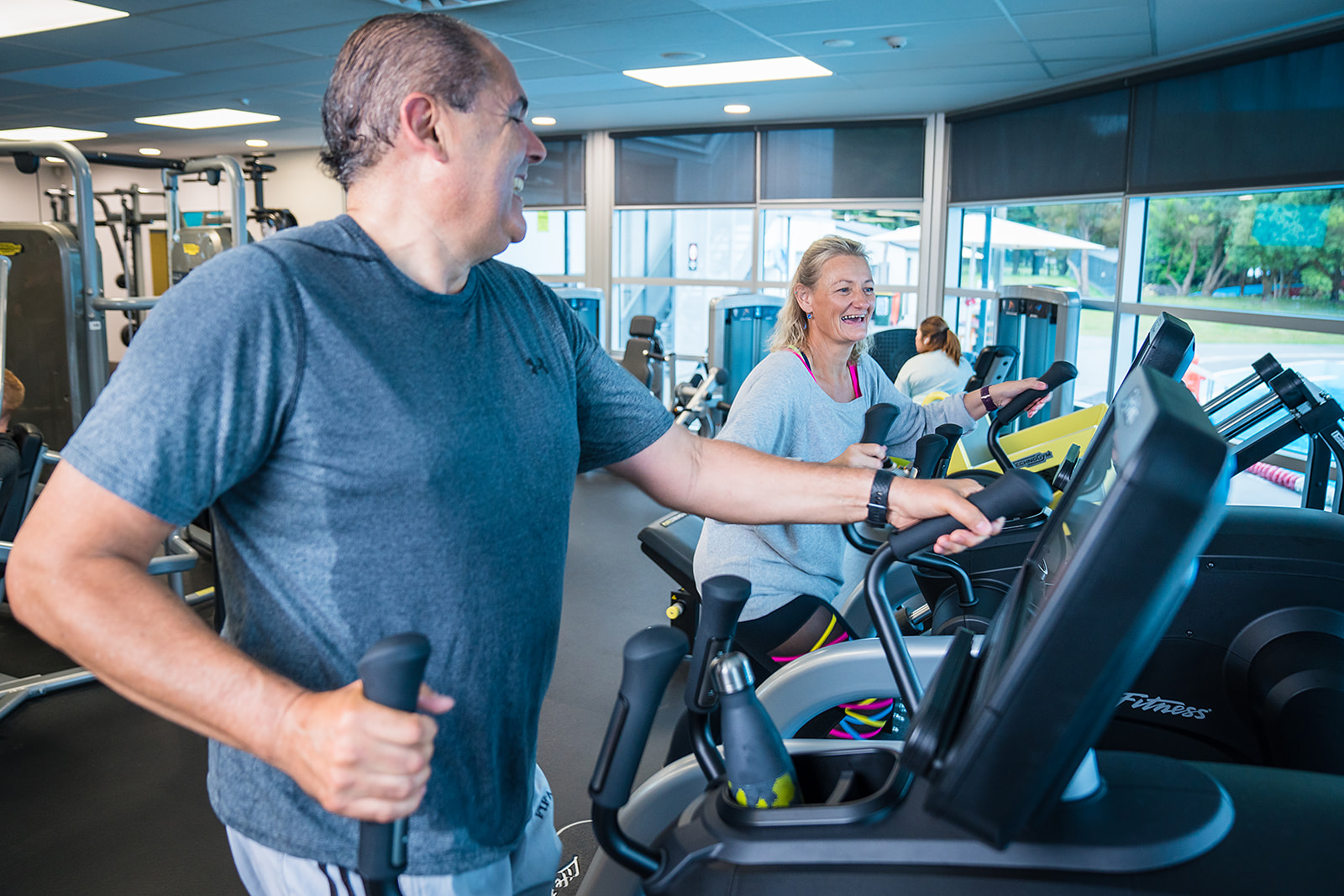 A smiling man and woman participating in an elliptical workout at Christchurch Recreation and Sport Centre. 