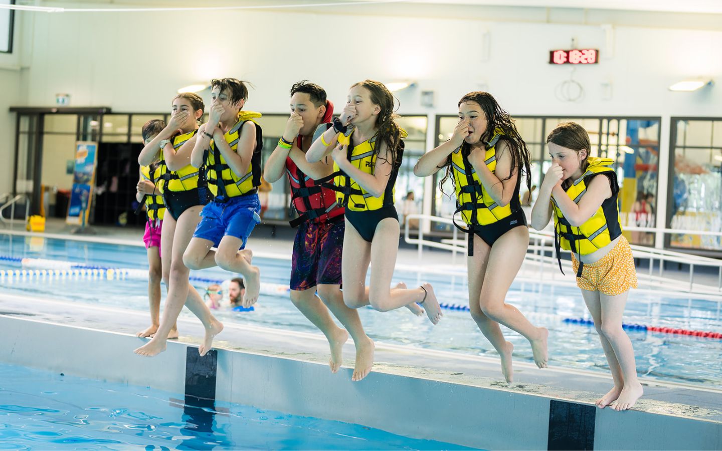 A group of children in yellow life jackets jumping into the water at Christchurch Recreation and Sport pool. 
