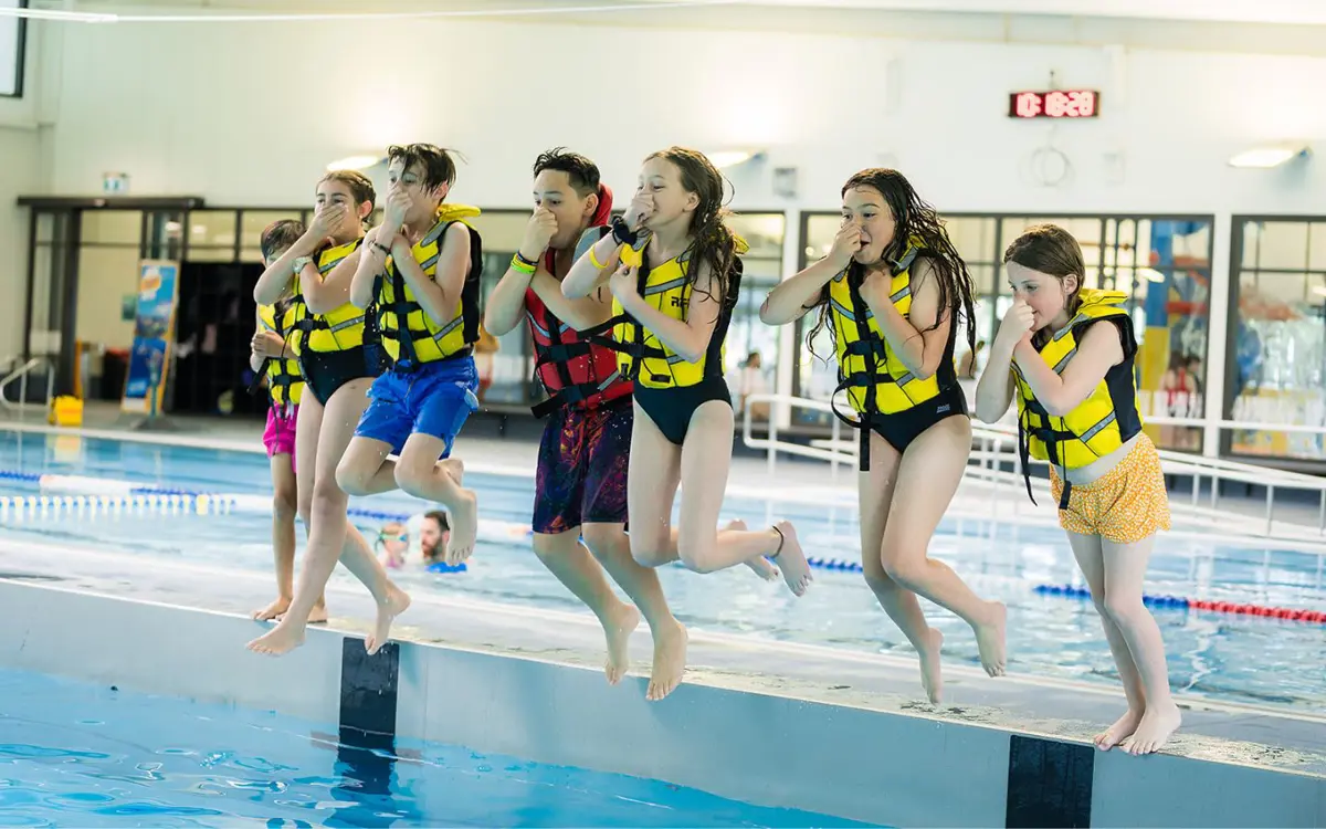 A group of children in yellow life jackets jumping into the water at Christchurch Recreation and Sport pool.