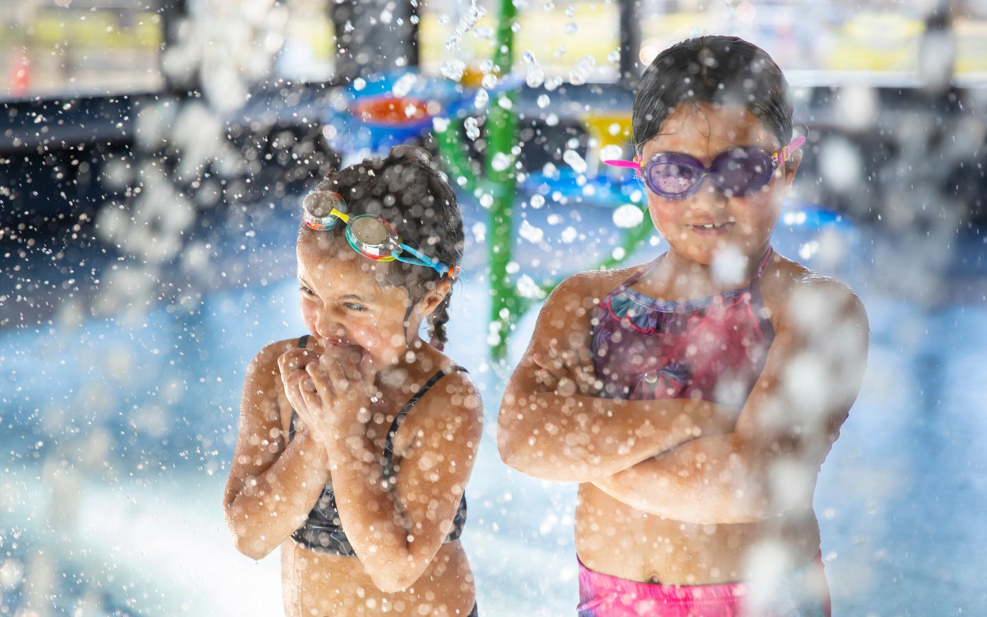 Two smiling girls playing in the toddler pool wearing goggles at the Christchurch Recreation and Sport pool. 