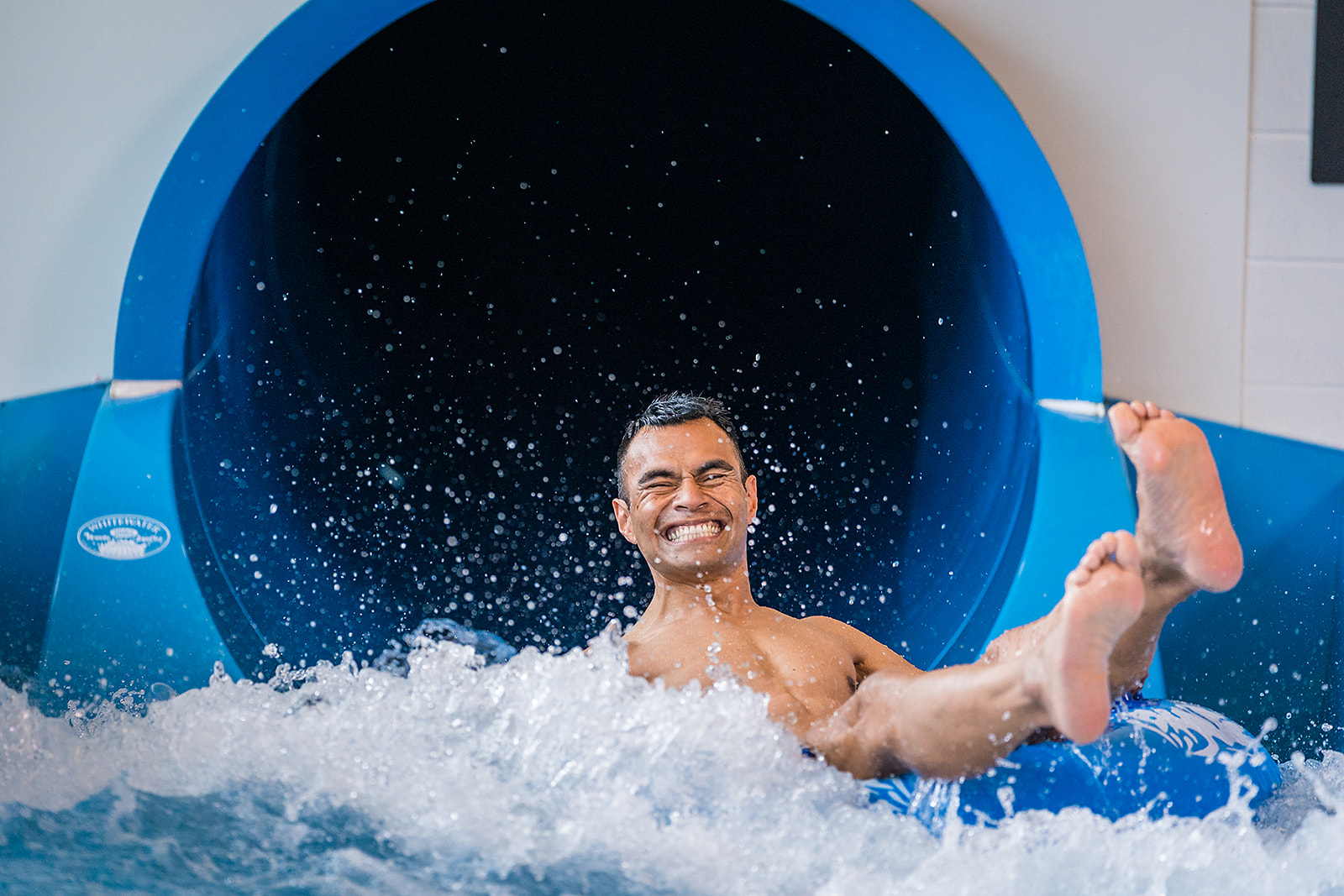 A smiling man enjoying the blue hydroslide at Taiora QEII Recreation and Sport pool. 
