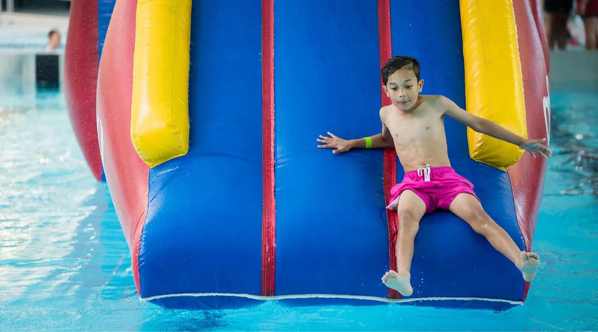 A boy sliding down an inflatable red, yellow and blue slide 1into the Hornby Rec and Sport Centre pool.