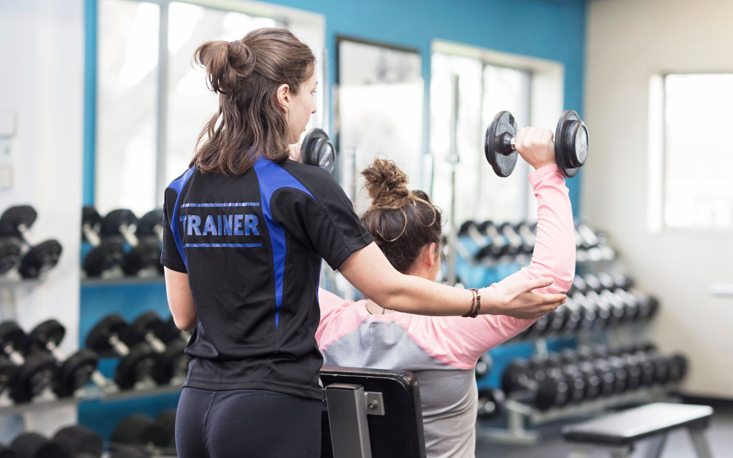 A female personal trainer in a blue and black shirt guiding a woman through an arm workout at Christchurch Recreation and Sport centre. 