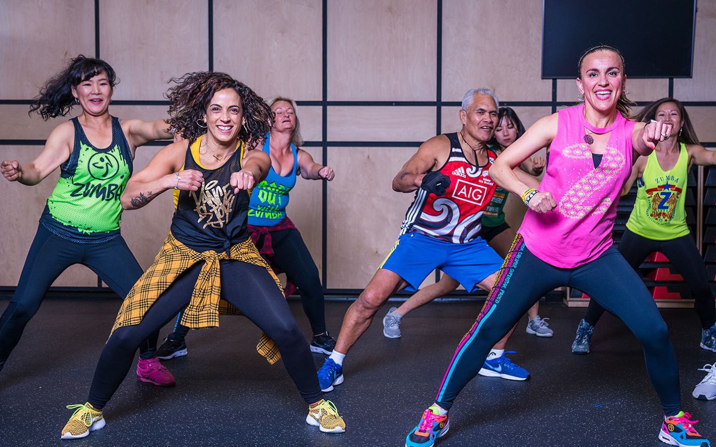 A group of smiling women and men in brightly dressed active wear dancing during a Zumba class at Christchurch Recreation and Sport.