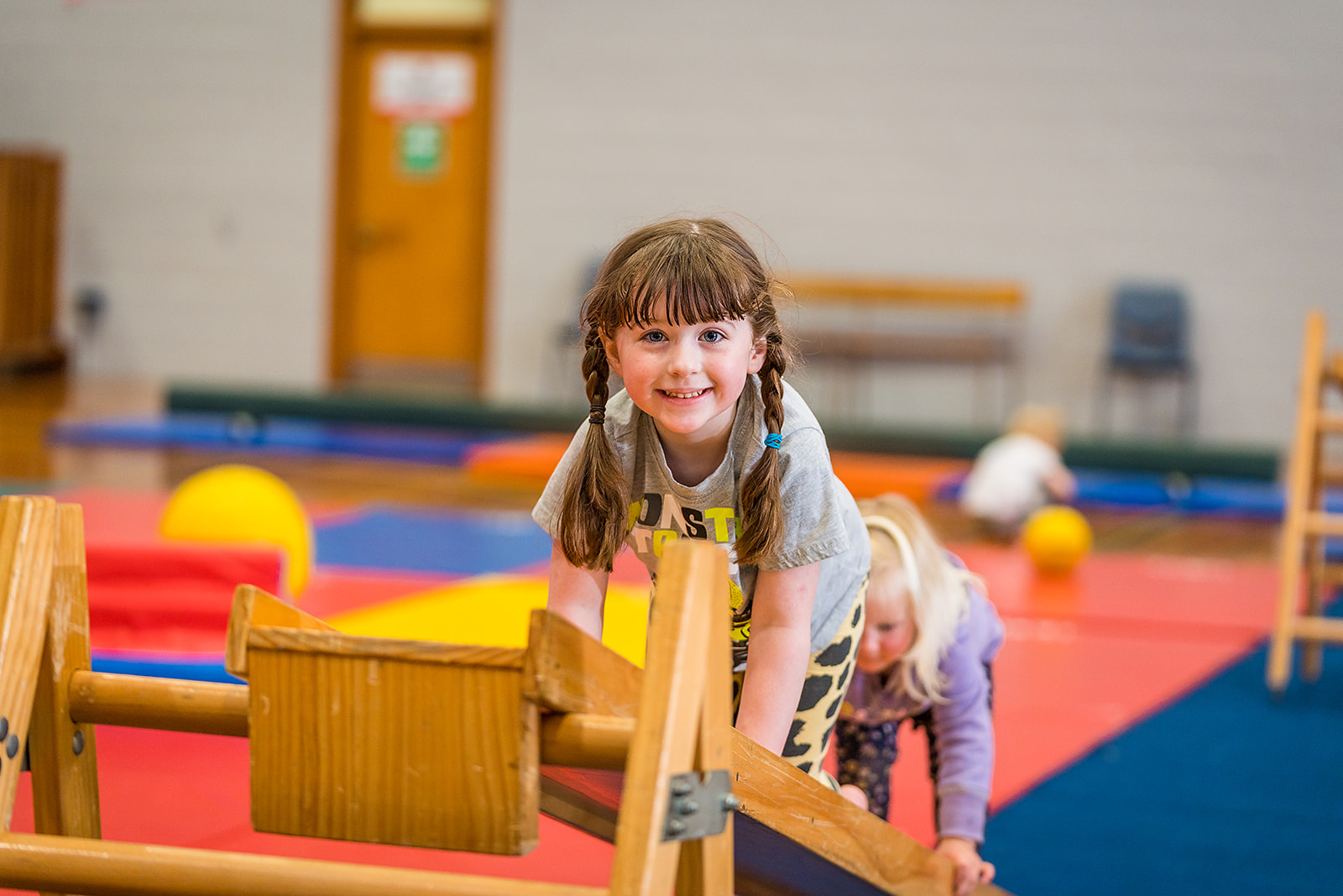 A smiling little girl climbing over a wooden ladder during a Tumbletimes class at Christchurch Recreation and Sport Centre