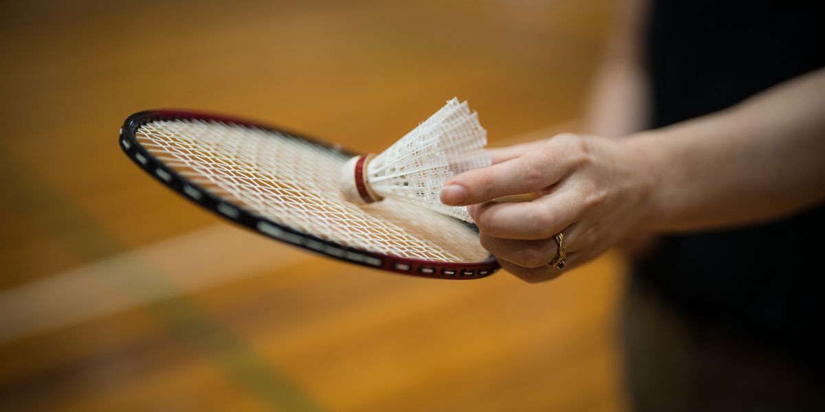 A person holding a badminton racket and a white birdie. 