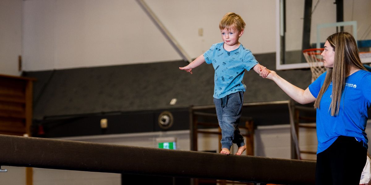 An instructor helping a child walk on a balance beam during a pre-school gymnastics class at Christchurch Recreation and Sport centre. 