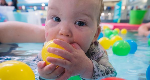 A baby holding a yellow floating ball while on their stomach during a swim class at Pioneer Recreation and Sport centre. 