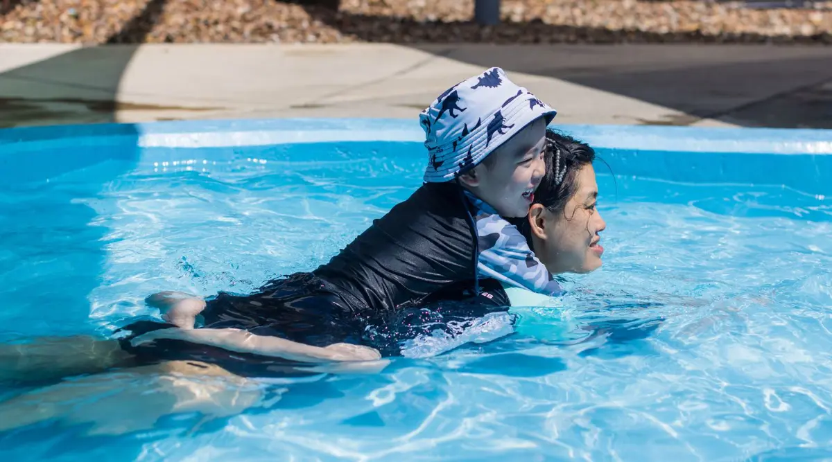 A little boy sitting on the back of an older boy in the toddler pool at the Halswell Summer pool.
